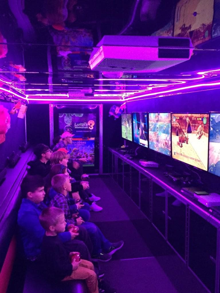 Kids seated together playing games in a purple-lit trailer